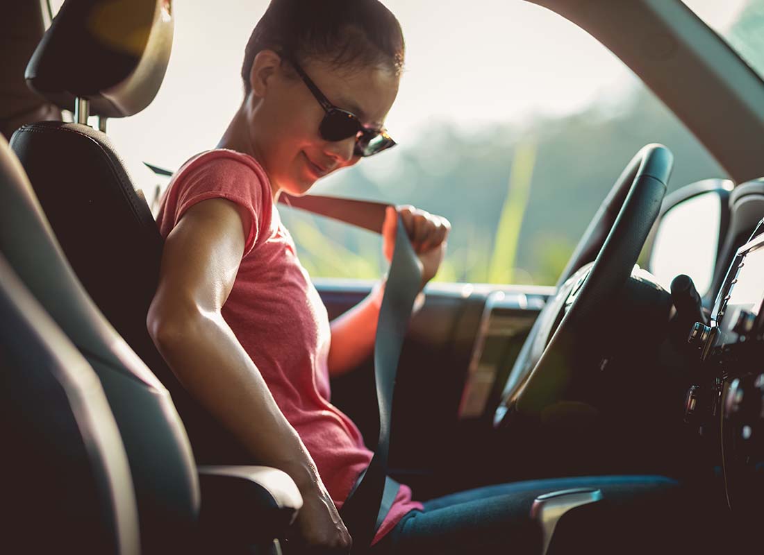 ERIE YourTurn Insurance - Young Woman Driver Buckling up Her Seat Belt Before Getting Ready to Drive Her Car on a Sunny Day at Sunset