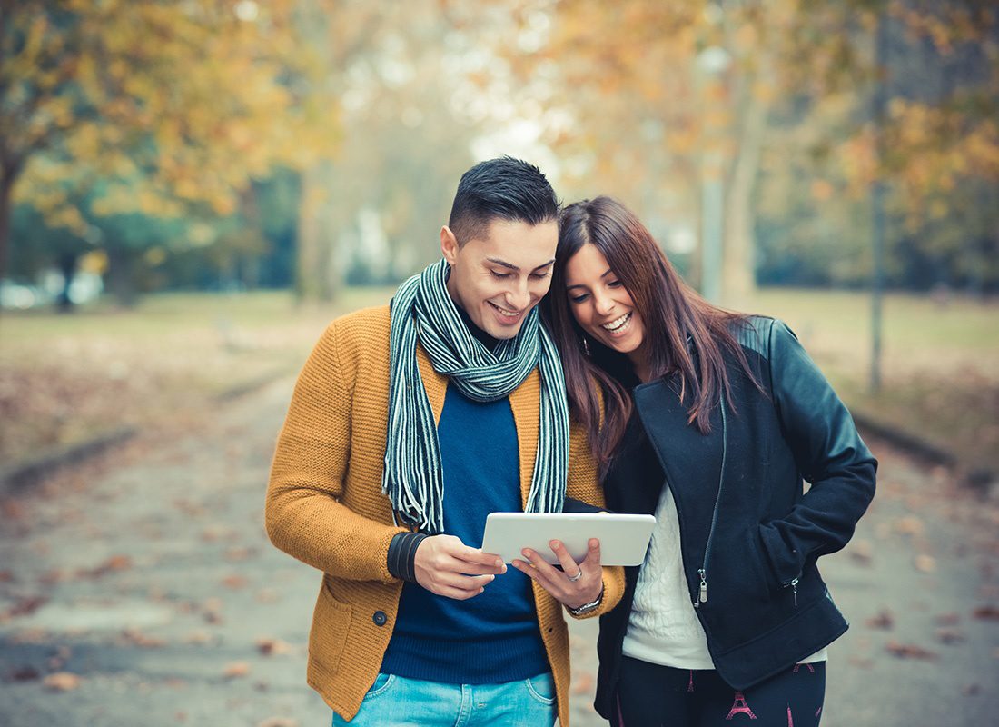 Read Our Reviews - Portrait of a Cheerful Young Couple Using a Tablet While Taking a Walk in the Park on a Brisk Fall Day
